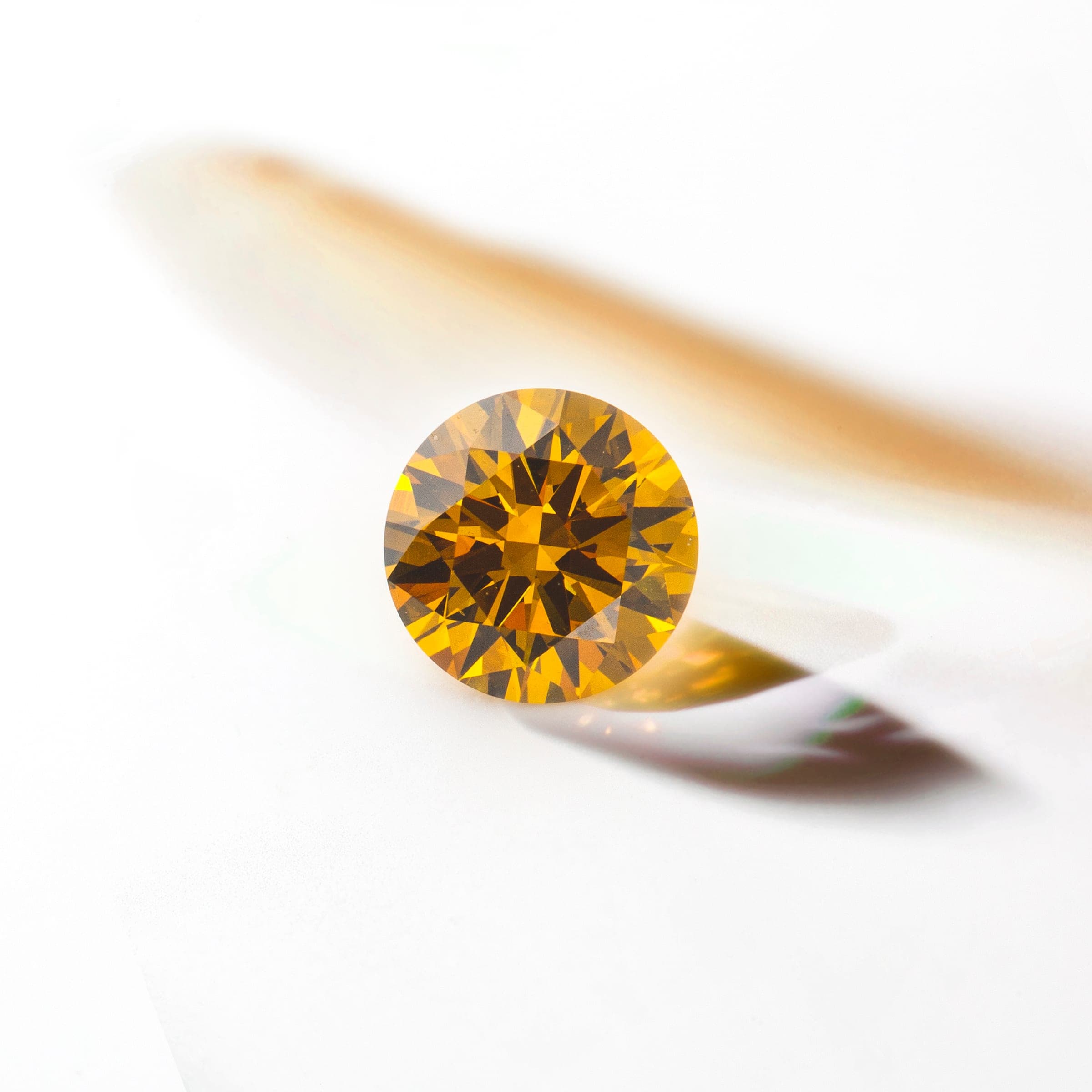 A yellow laboratory-grown diamond, brilliant cut, on a white background